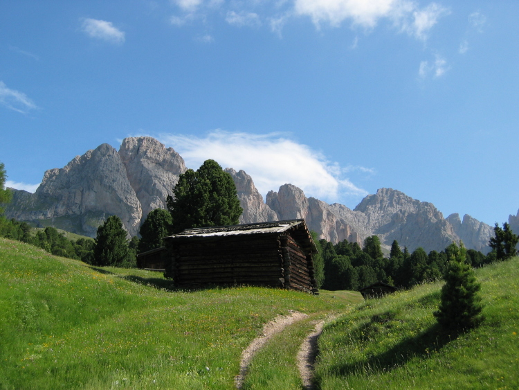 Una casetta di legno lungo il sentiero. Sullo sfondo le bianche montagne rocciose.