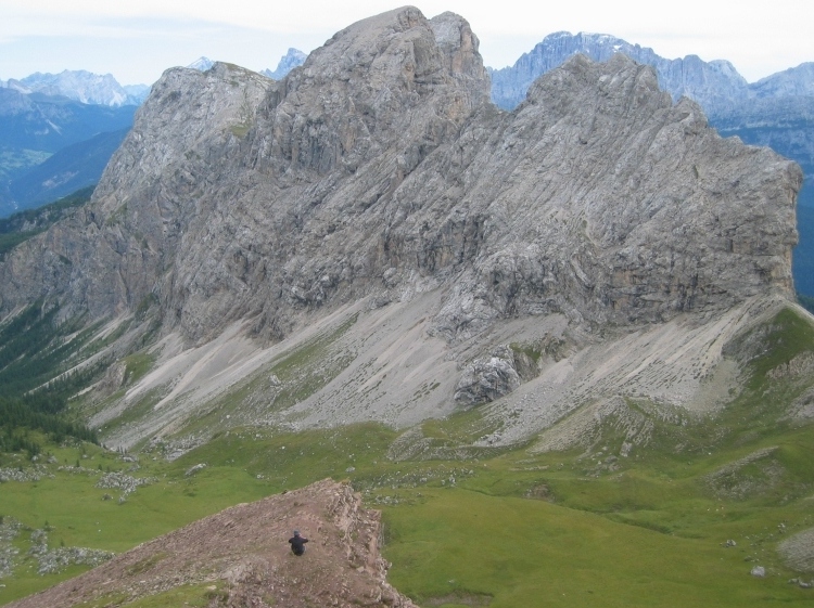 Un uomo è seduto su uno spuntone di roccia e guarda la montagna che ha di fronte.