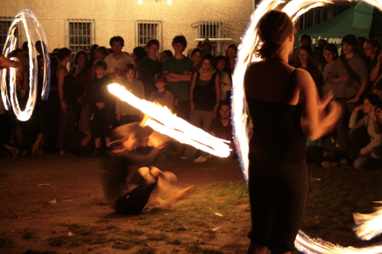 Una delle ragazze fa anche acrobazie mentre disegna col fuoco. Si siede, si alza, si sposta.