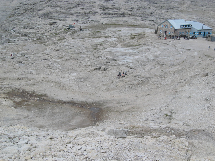 Dall'alto vediamo il rifugio Boè, piantato nella roccia. Qui faremo una sosta. Intorno al rifugio conche di terra scura, a volte c'è dell'acqua.