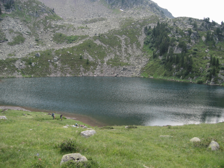 Il lago con l'acqua mossa dal vento. Sulla riva alcune persone che riposano su una coperta, altre che camminano con un bambino.