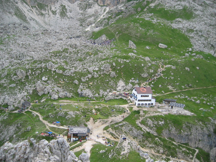 I rifugi Roda Di Vael e Pederiva visti dall'alto del Ciampac. Più in alto, in una conca, un gruppo di persone ascolta il concerto già iniziato.